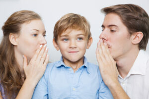 Parents whispering to smiling son covering mouth